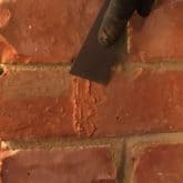 Picture showing brick being scraped following repair with crack repair injection mortar